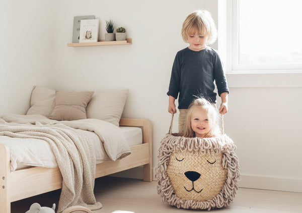 Two young children playing with the Bellybambino Lion basket, hand-tufted wool mane and embroidered face, in a bright family bedroom.