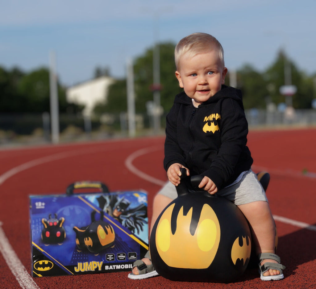 confident toddler riding a vibrant batmobile hopper toy indoors