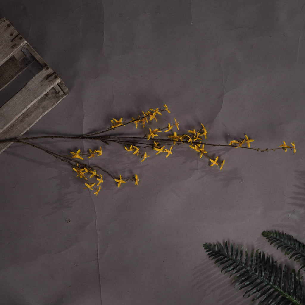 a soft-focus close-up of vibrant yellow forsythia blossoms on a realistic artificial stem