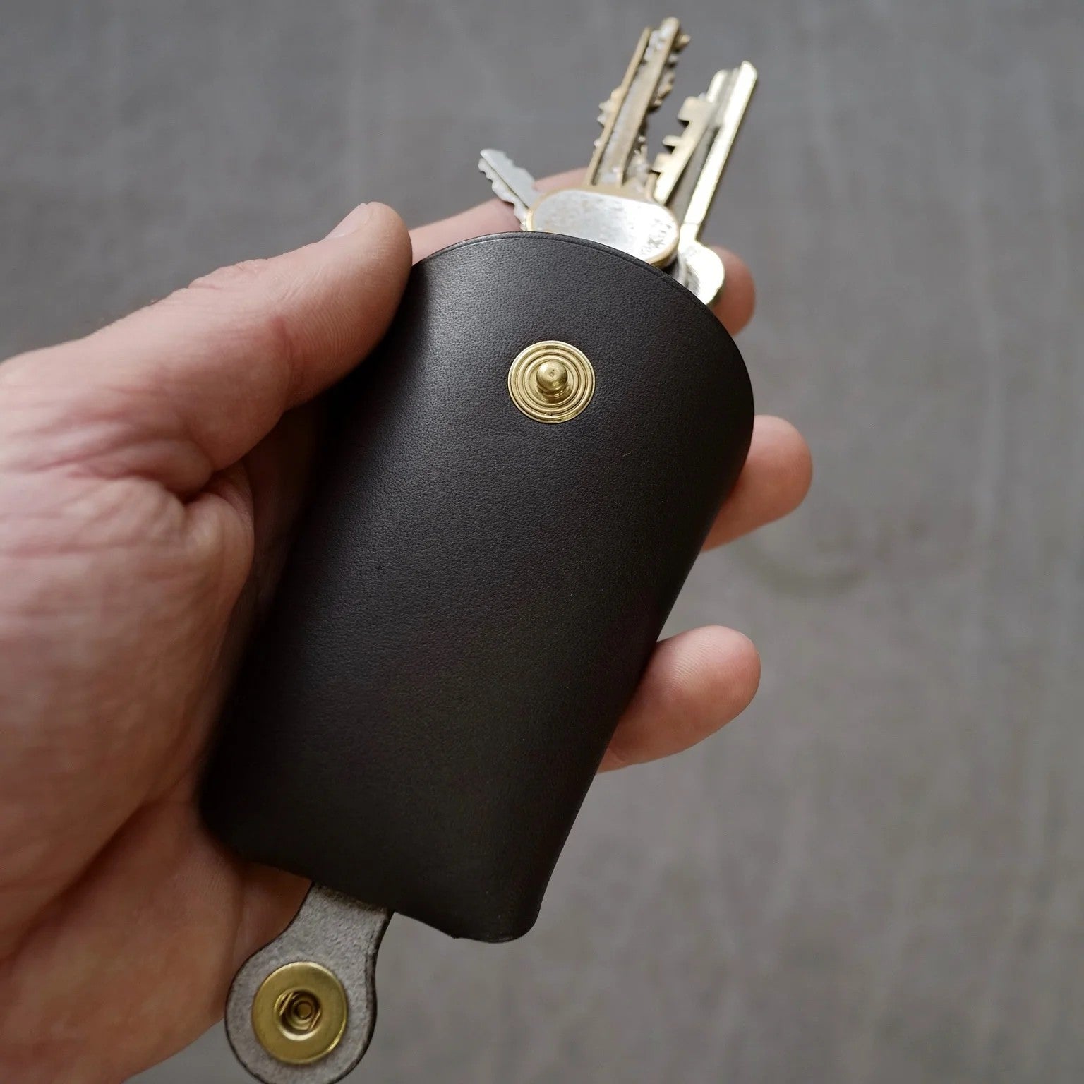 bold black italian leather keyholder open on a dark marble surface, showcasing its folded construction