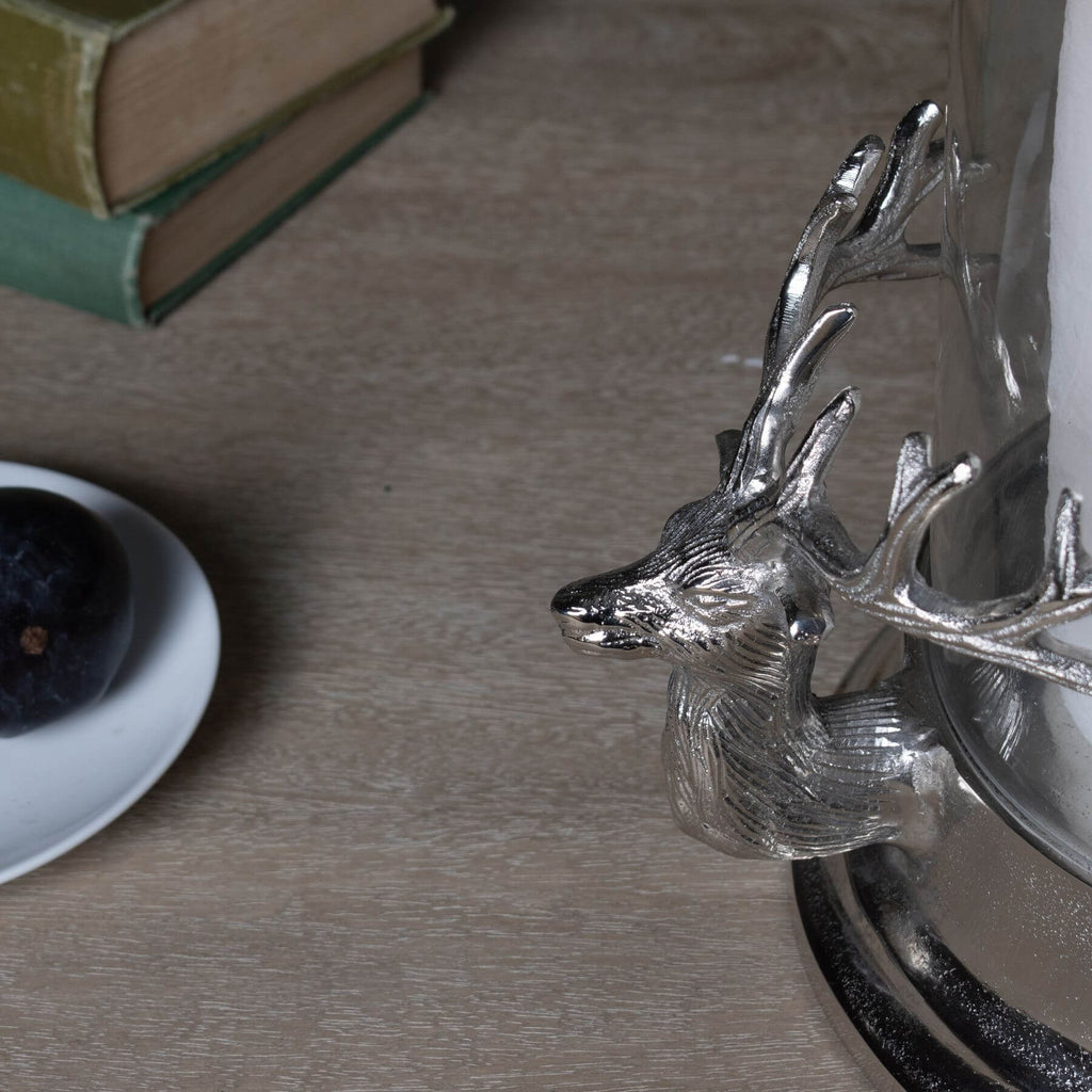 Silver stag heads hurricane lantern with glass cylinder, polished metal finish, and intricate woodland-inspired details. by sostter at brixbailey.com