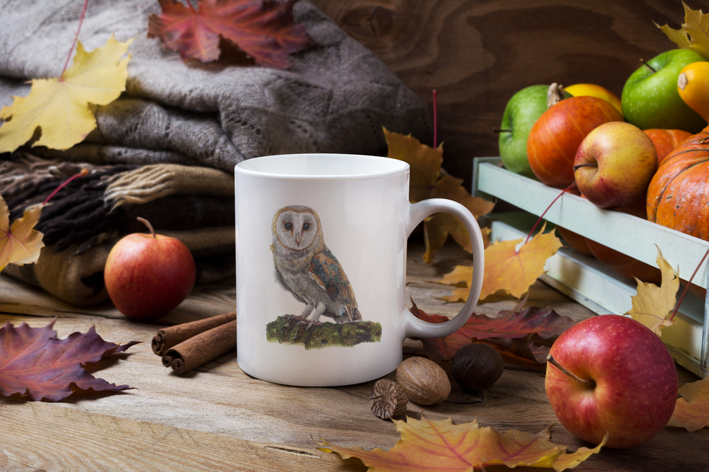 White mug with an owl design on a wooden surface with autumn leaves and fruits.