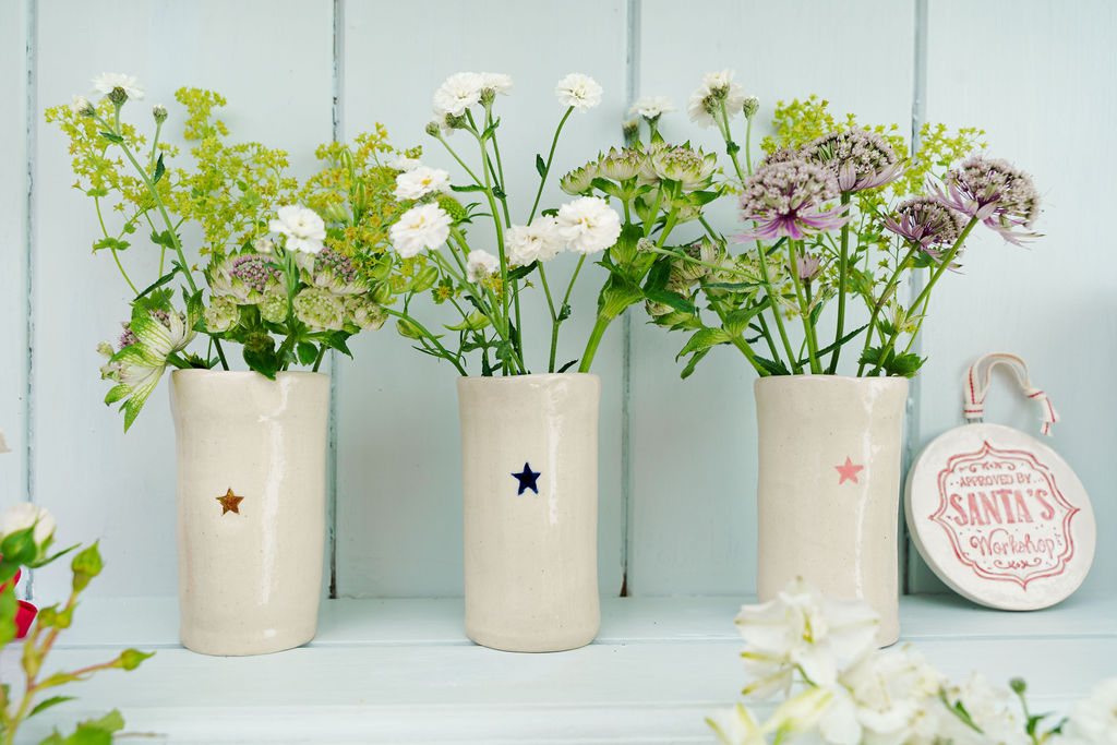 Three ceramic vases with floral arrangements on a light blue wooden shelf. by Sea Bramble Potter at Sostter