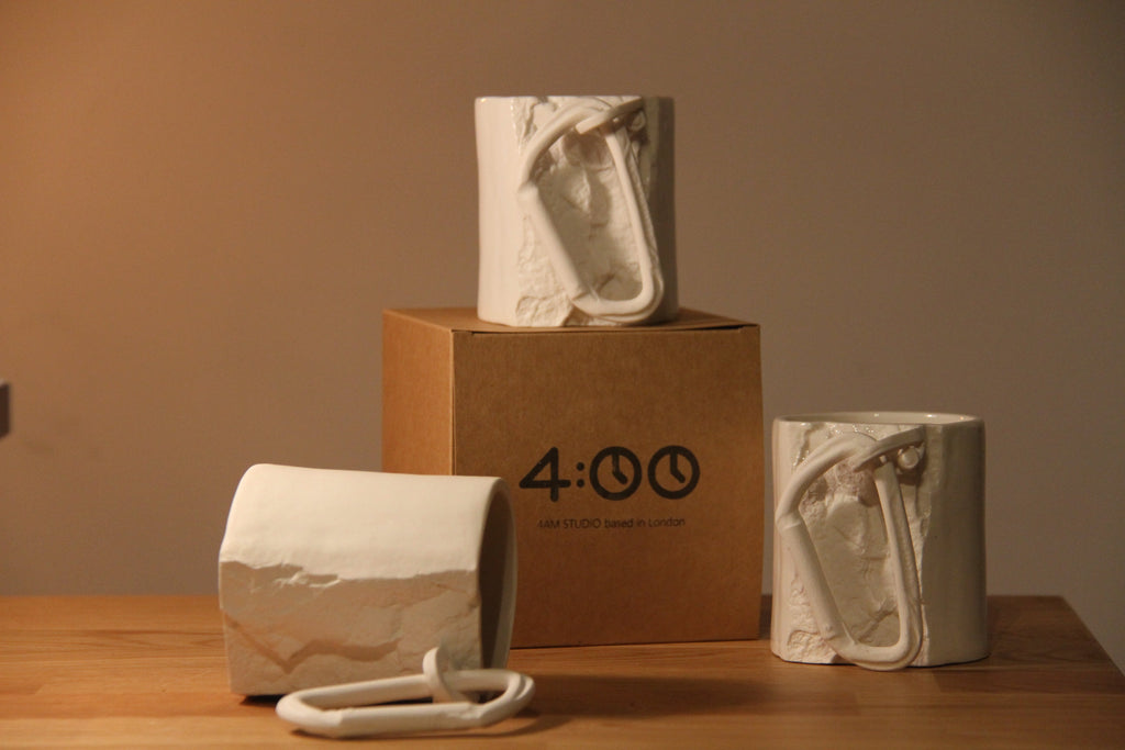 Three ceramic sculptures on a wooden surface with a cardboard box displaying '4:00'. 4am studio at Sostter