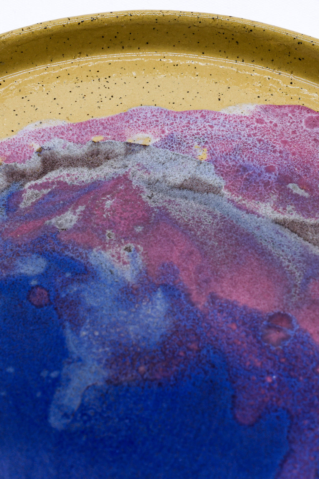 Close-up of a ceramic plate with a colorful, marbled design on a speckled beige background.