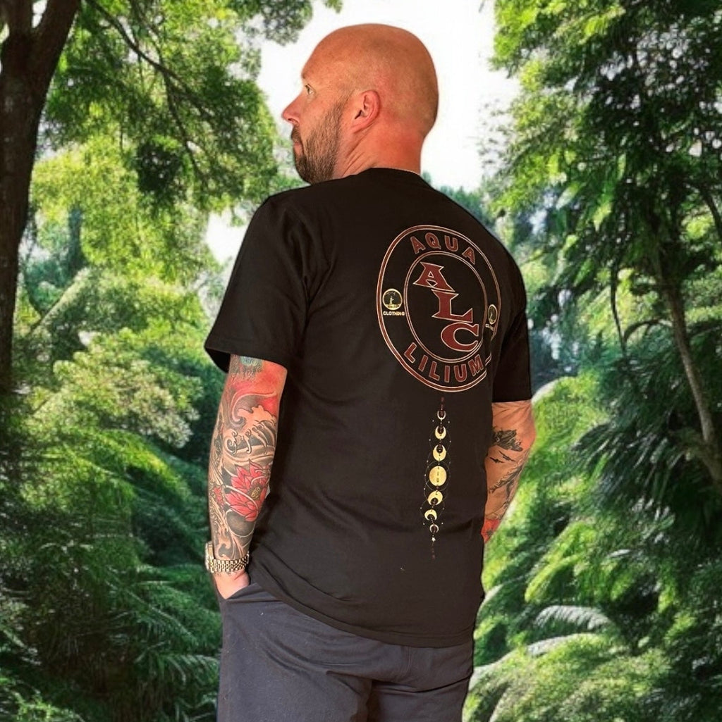 Man wearing a black t-shirt with a logo on the back, standing in a forest on rokkatei-eshop.mom