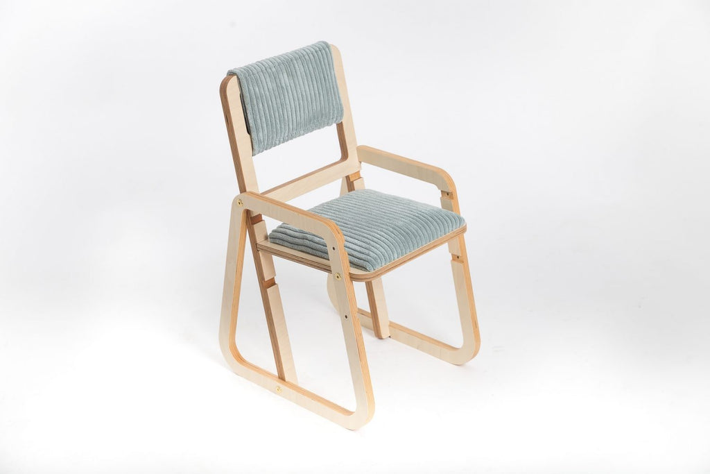 mint green julle kids chair in a bright playroom, showcasing its smooth birch wood grain and plush padding