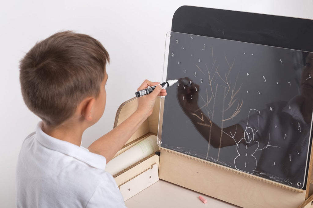 a child's hand drawing on the mint green montessori table's chalkboard surface