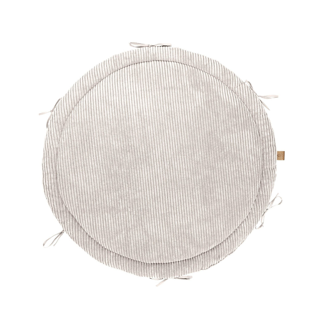 a soft vanilla baby nest with a plush braided bumper on a cozy nursery rug