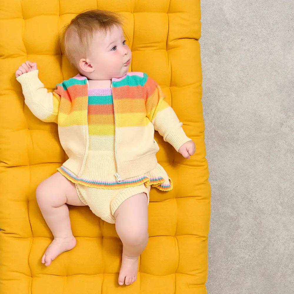 Baby in a colorful outfit sitting on a yellow cushioned surface