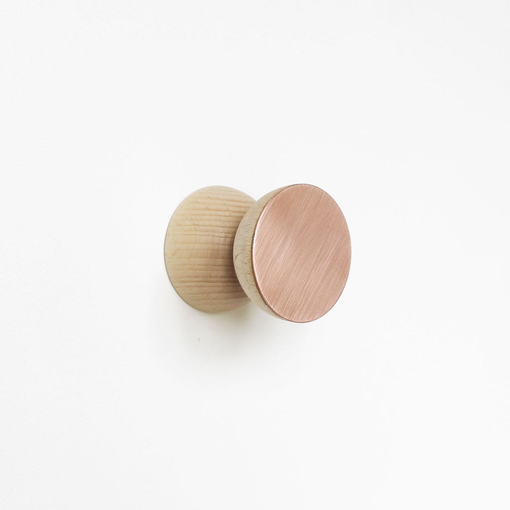 close-up of a solid beech wood wall hook with brushed copper finish mounted on a cabinet
