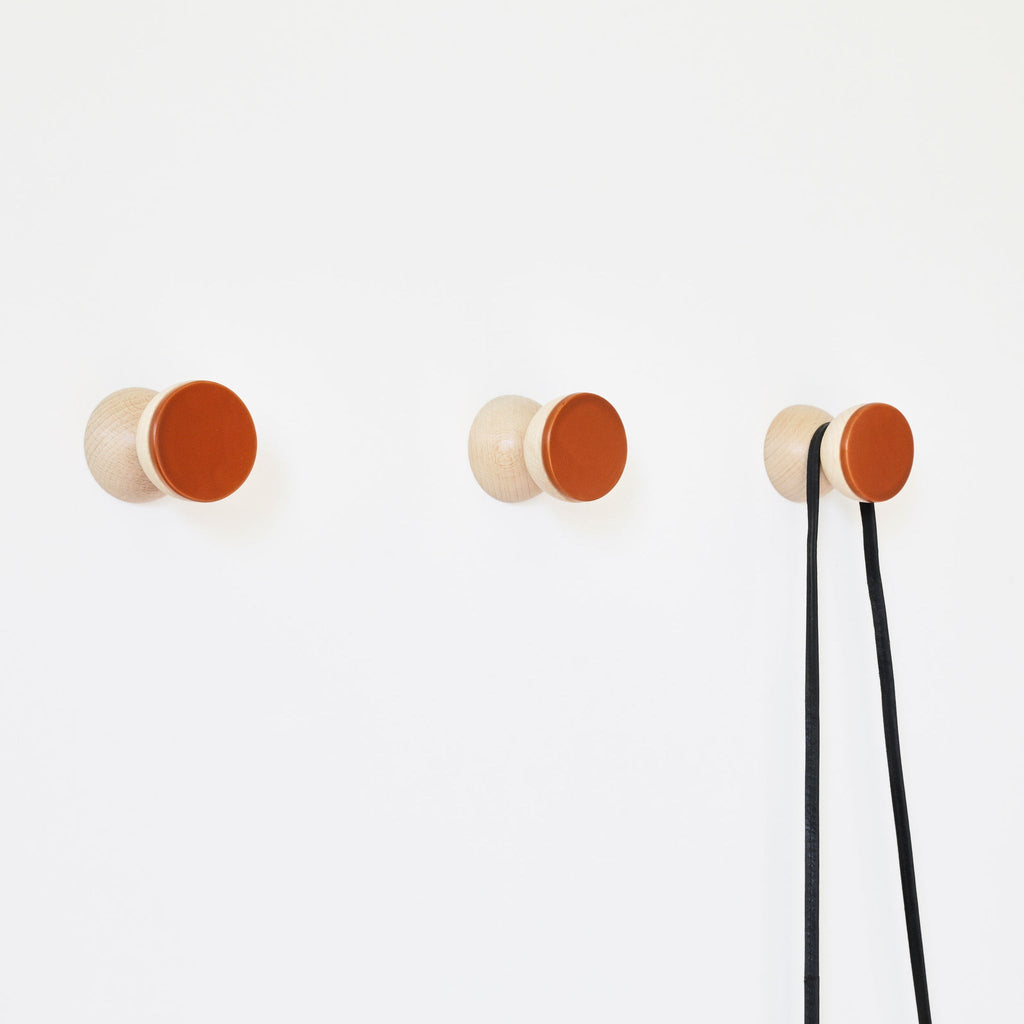 bold dark terracotta ceramic wall hook on rustic wood in dramatic studio lighting