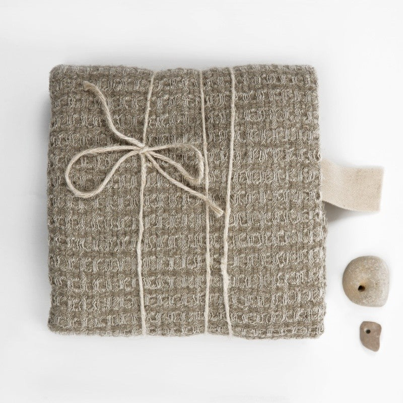 a textured grey linen bath towel draped over a wooden stool in warm morning light