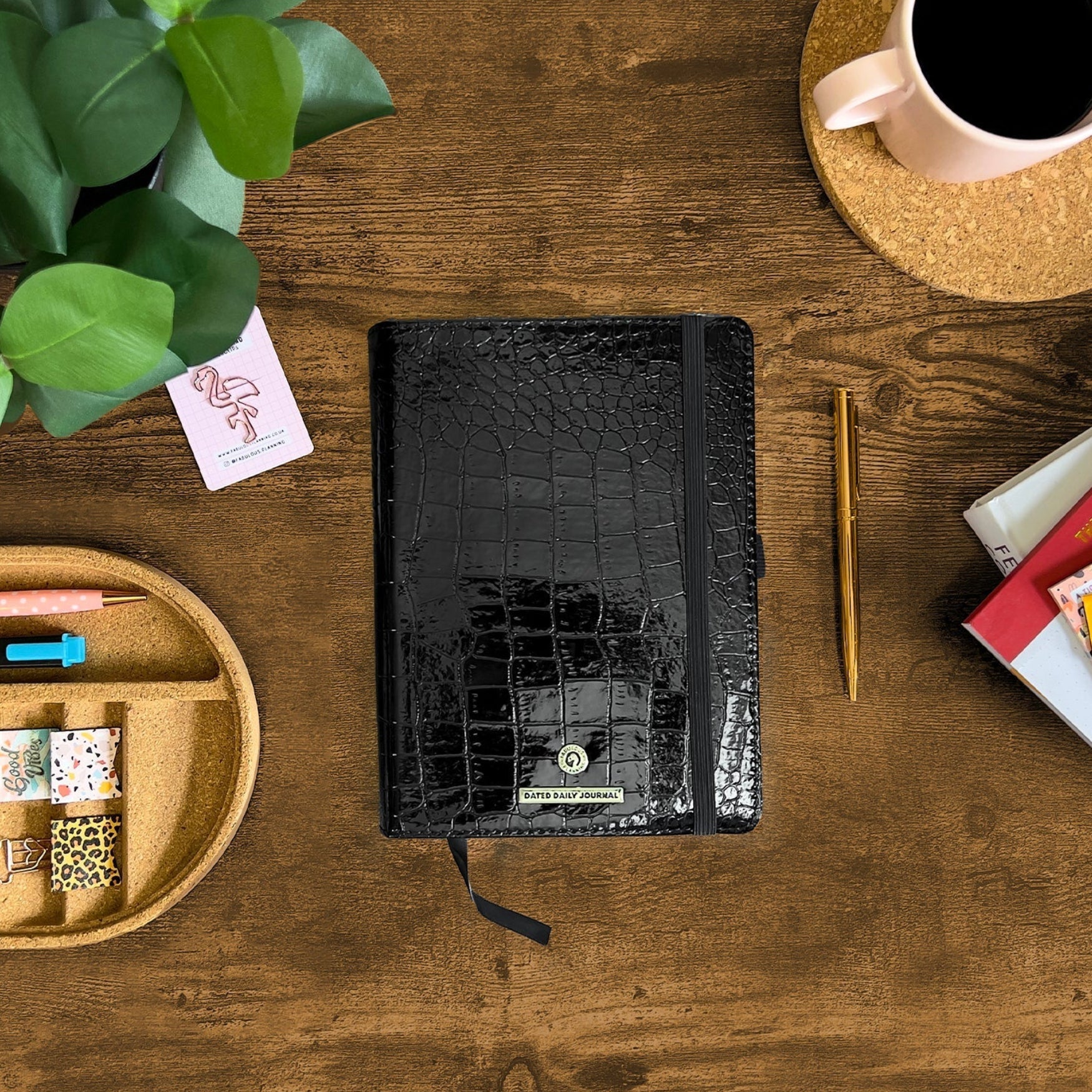 Black crocodile-patterned notebook on a wooden desk with a cup of coffee, pen, and small items on Sostter