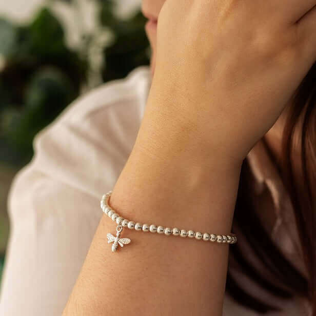 Silver bracelet with a dragonfly charm on a wrist against a blurred background at Sostter