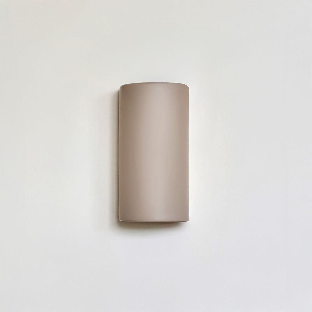 handmade taupe ceramic wall light casting a soft, warm glow in a nursery
