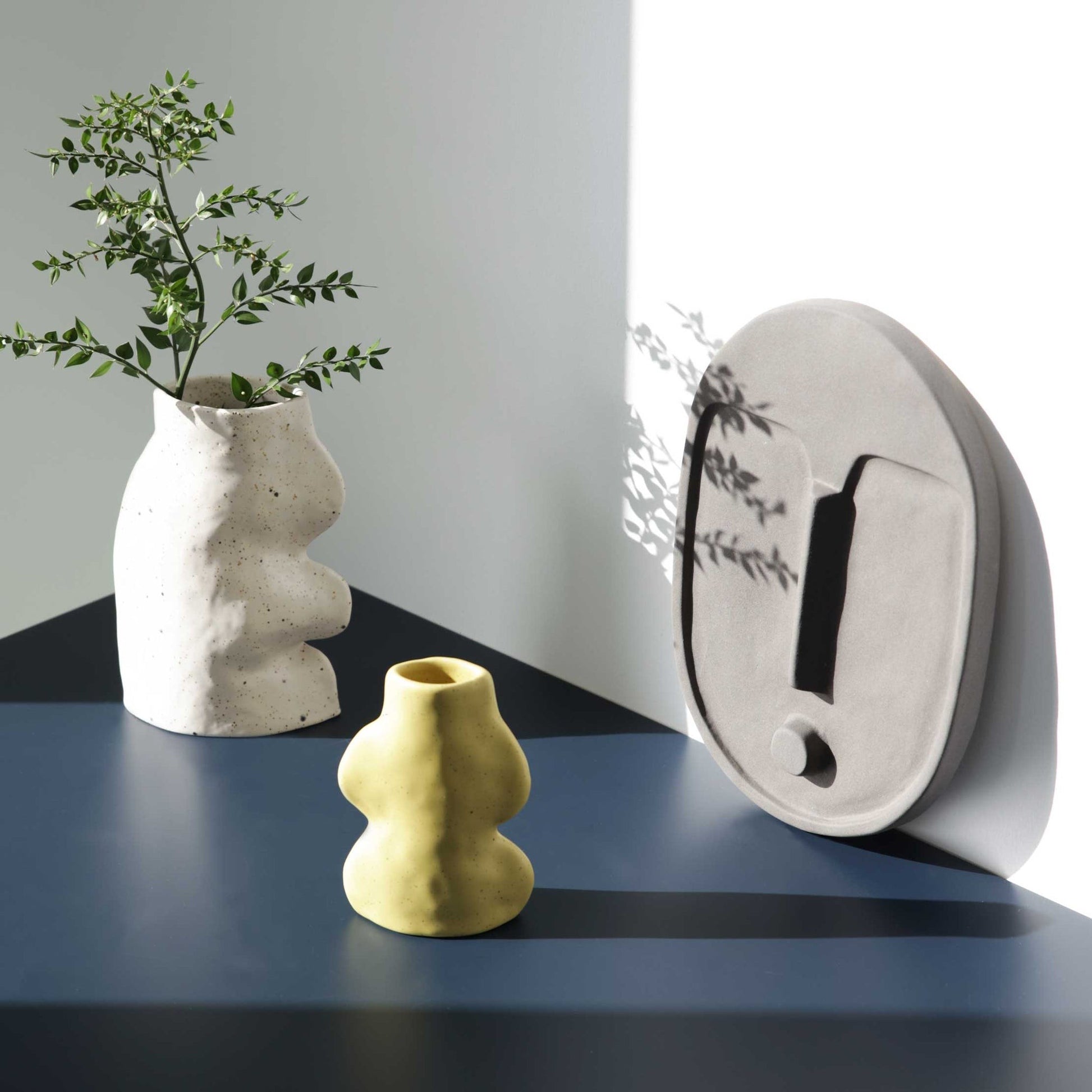 abstract ceramic wall mask in matte terracotta orange, side-lit to highlight its textured artisan finish