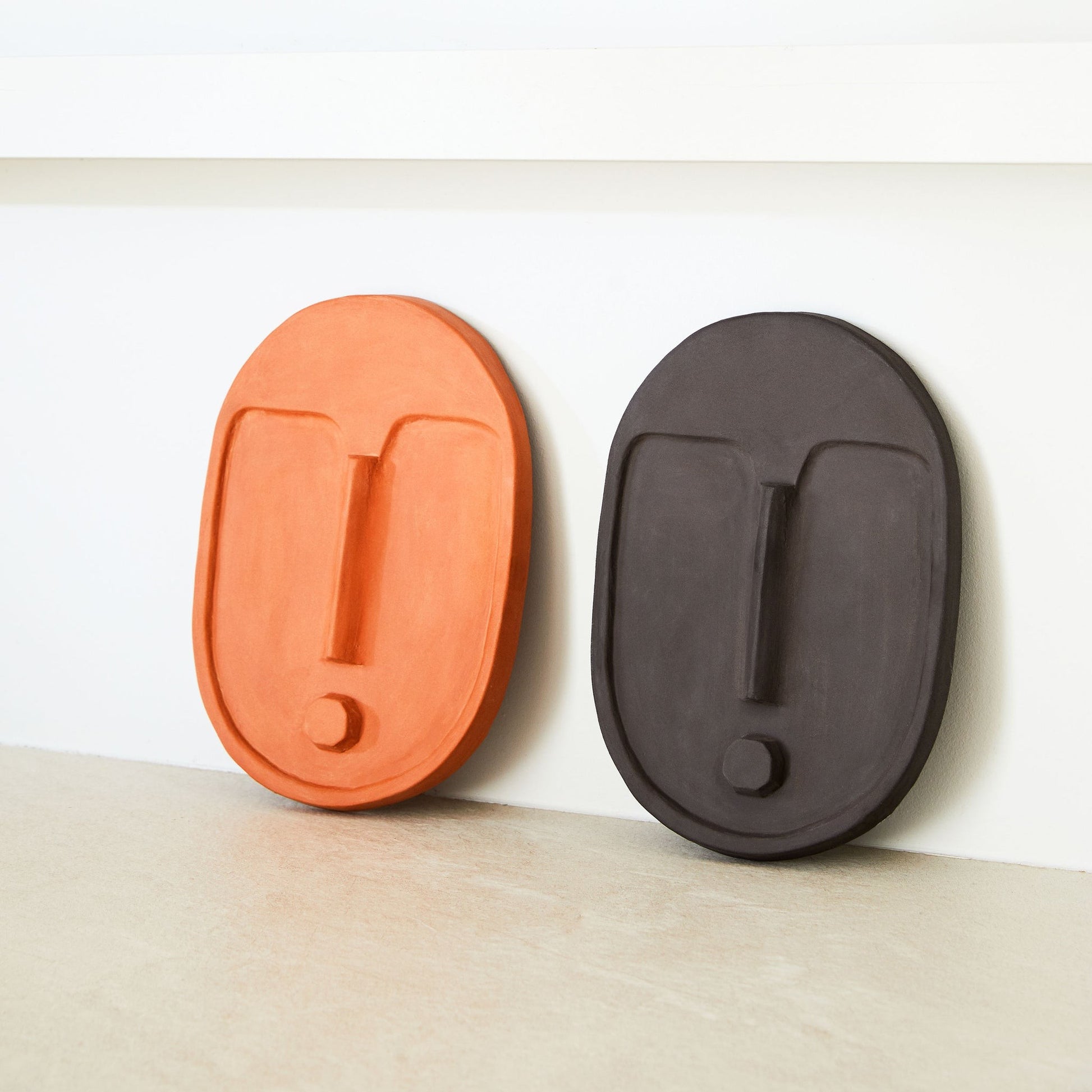 softly lit abstract ceramic wall mask with a warm terracotta glow on a cozy neutral wall