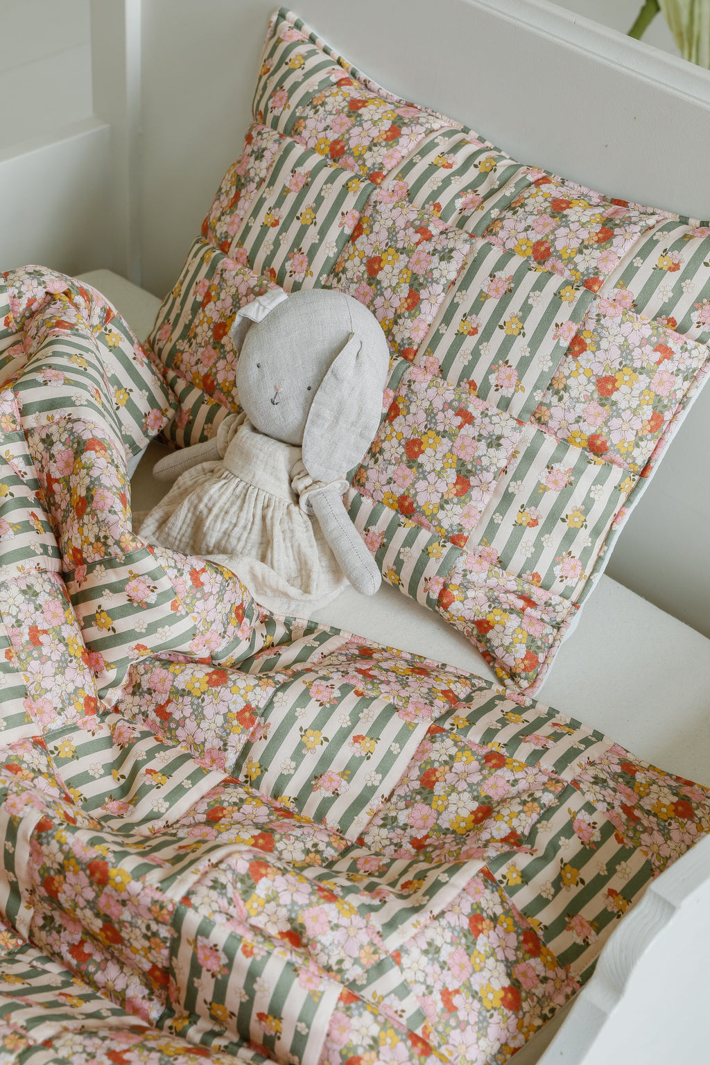 playful green garden cotton quilted blanket and pillow set laid out on a sunny nursery floor