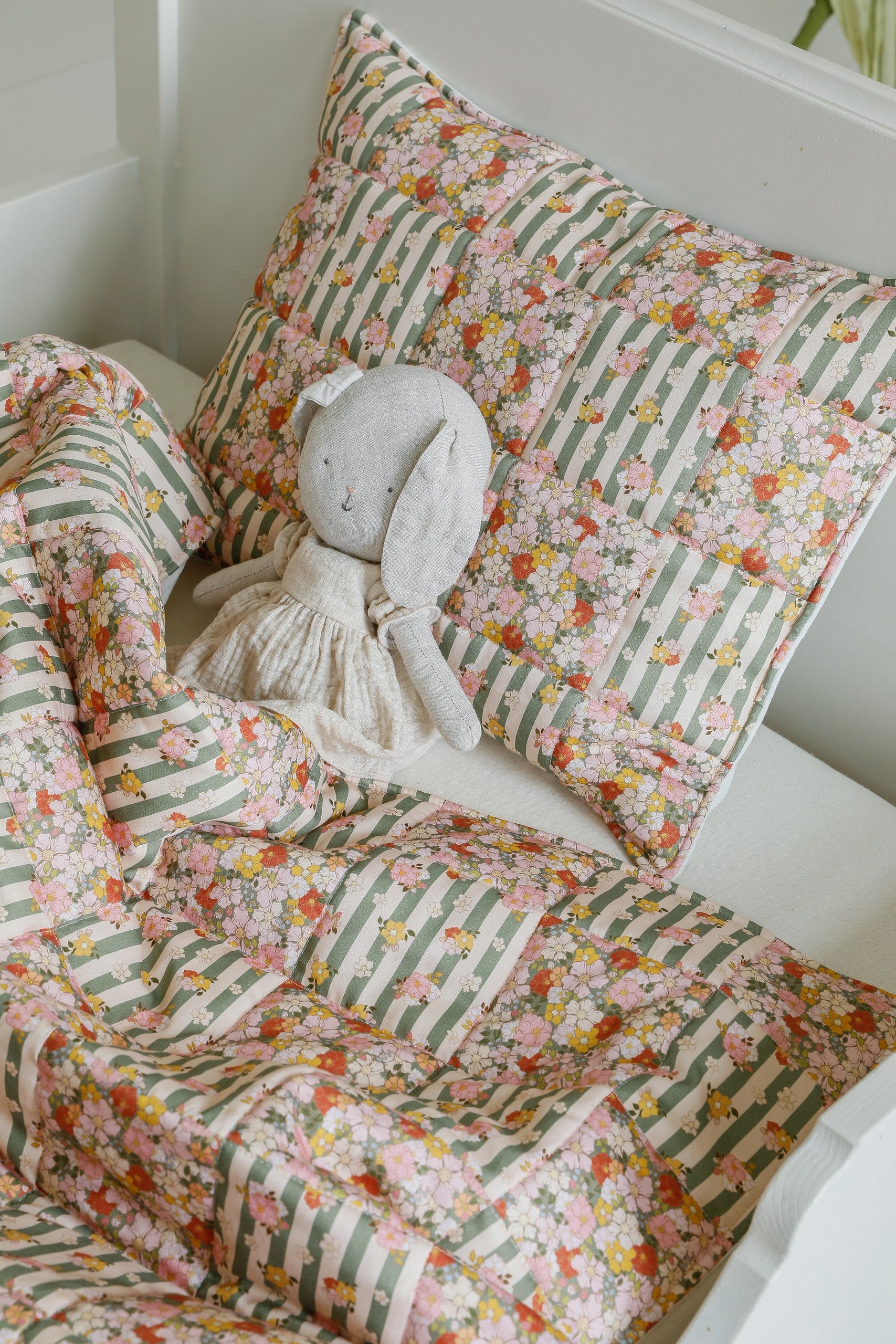 playful green garden cotton quilted blanket and pillow set laid out on a sunny nursery floor