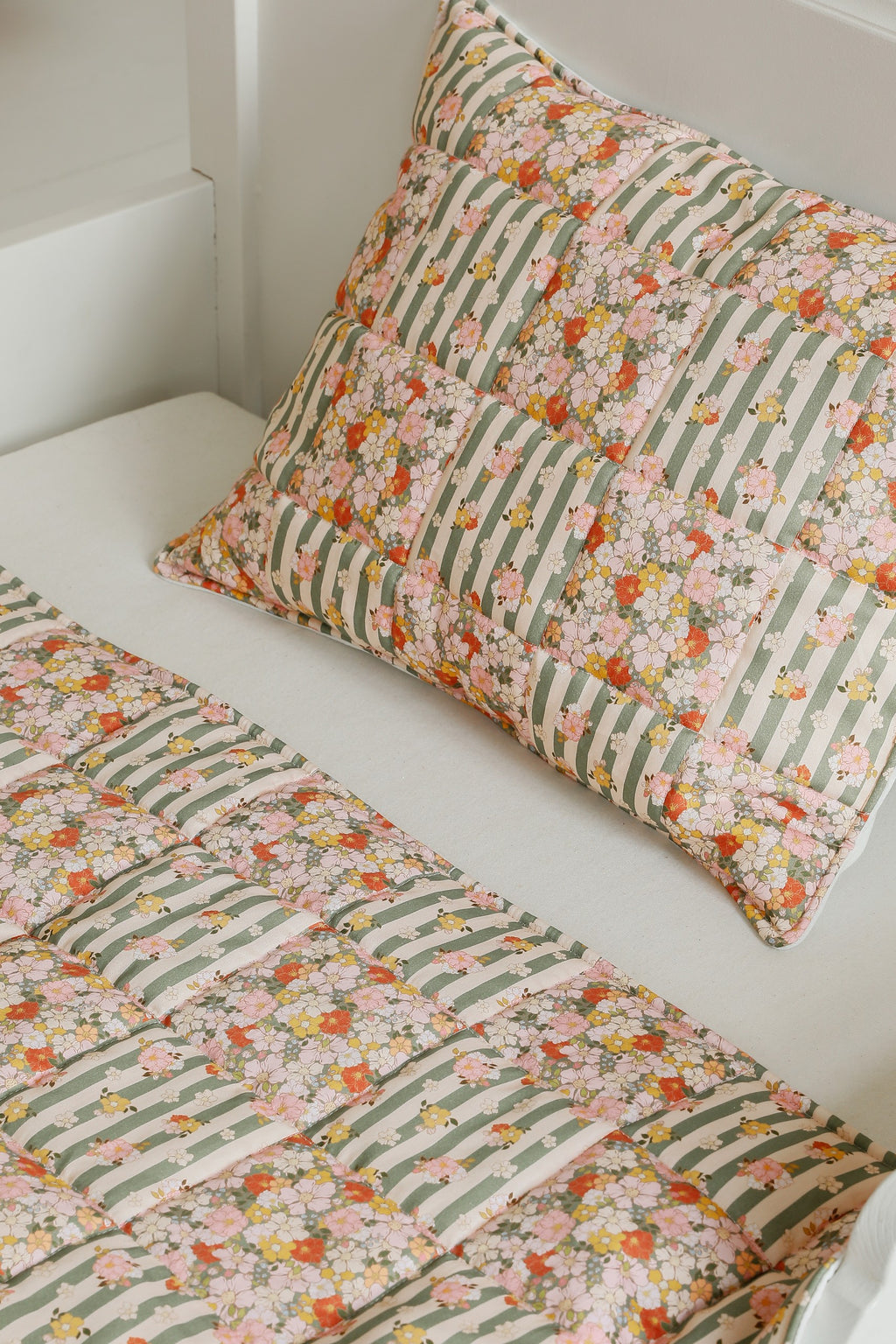 green garden cotton quilted blanket and pillow set laid flat on a wooden floor, showcasing its soft patchwork design