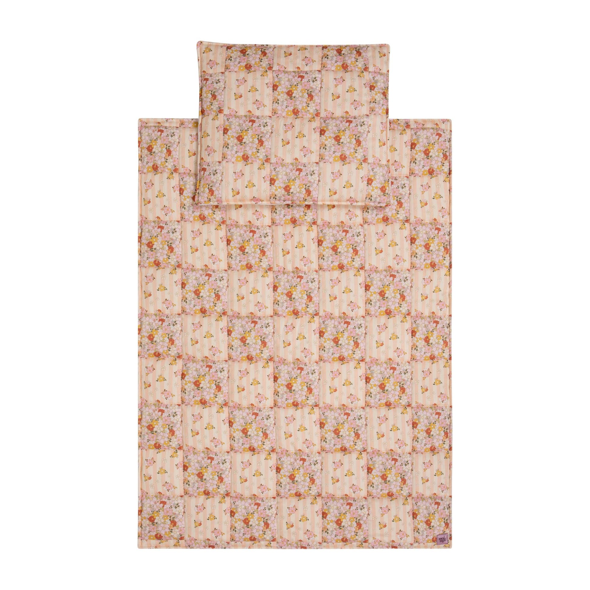 playful spring garden cotton quilted blanket and pillow set laid on grass, bright patchwork patterns under sunlight