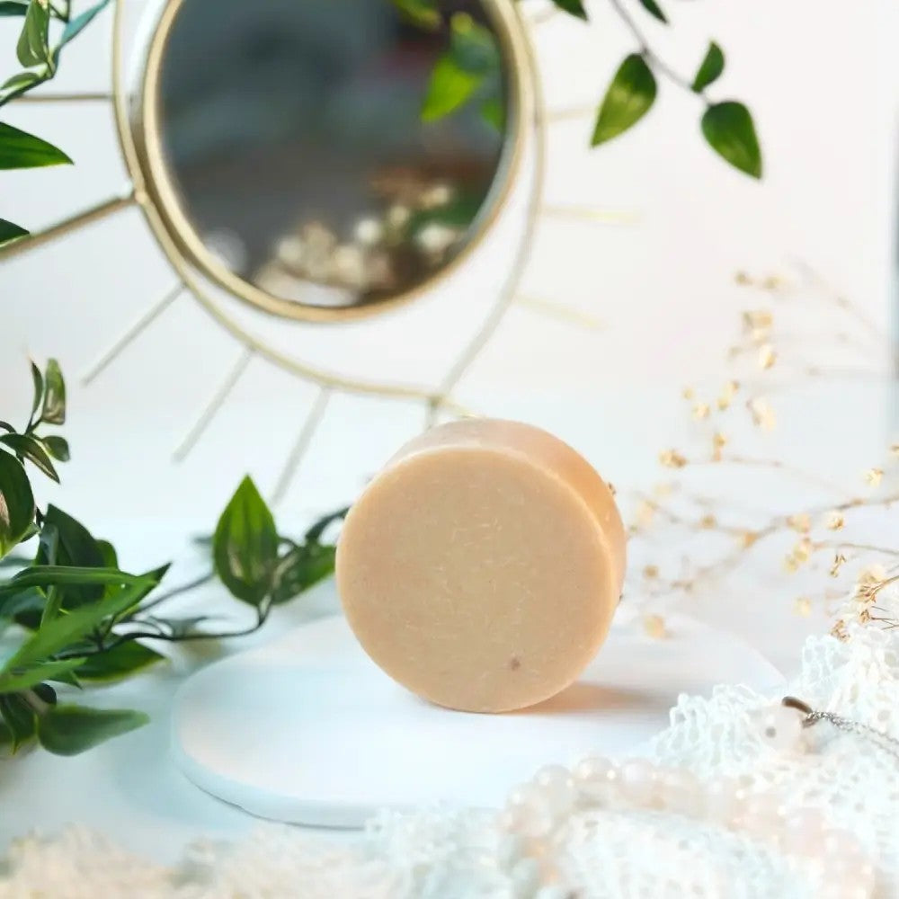 pink clay face cleanser bar with orange aroma, vegan and cruelty-free, resting on a wooden tray