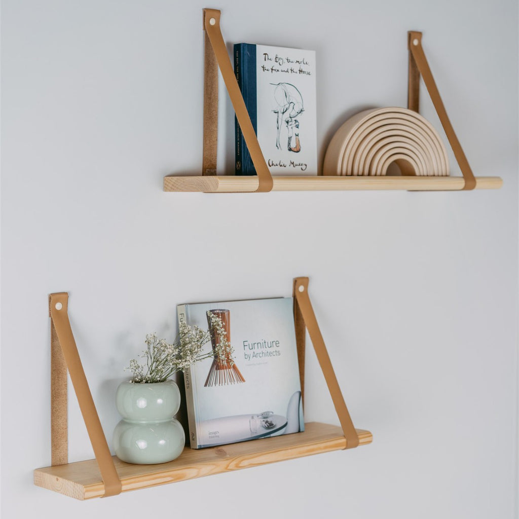 a nursery's floating pine shelf with soft leather straps holding a cozy baby blanket and a small plush toy