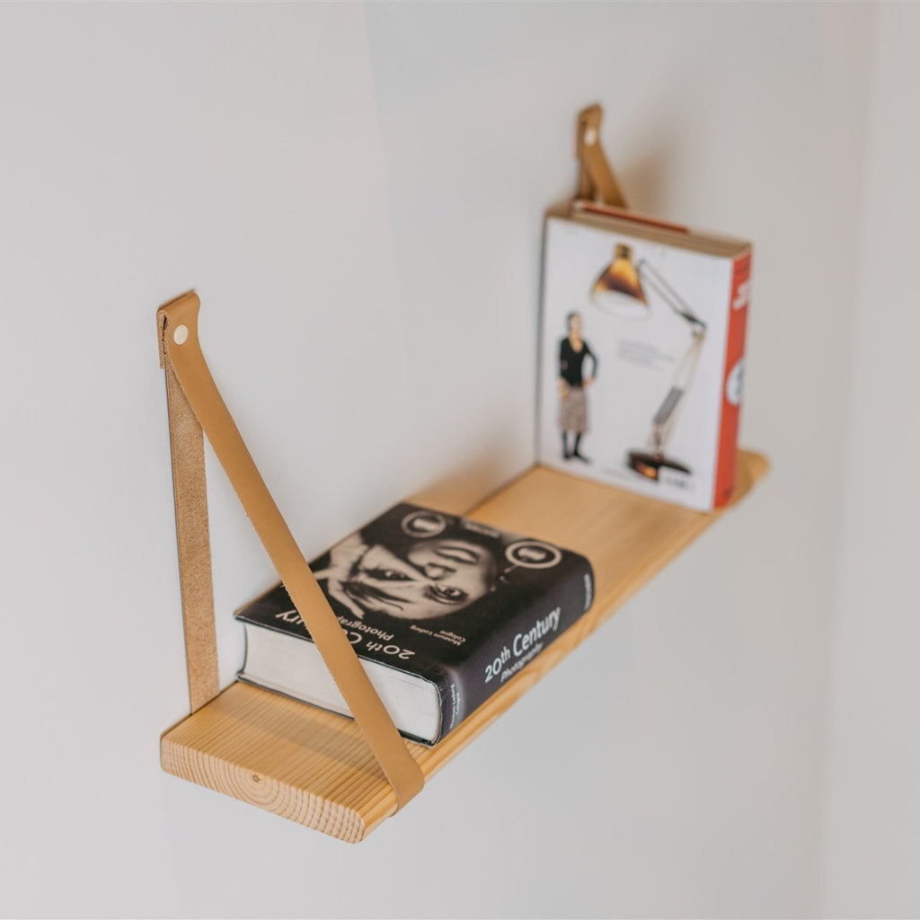 a soft-lit floating pine shelf with camel leather straps holding a cozy baby blanket and a small stuffed animal