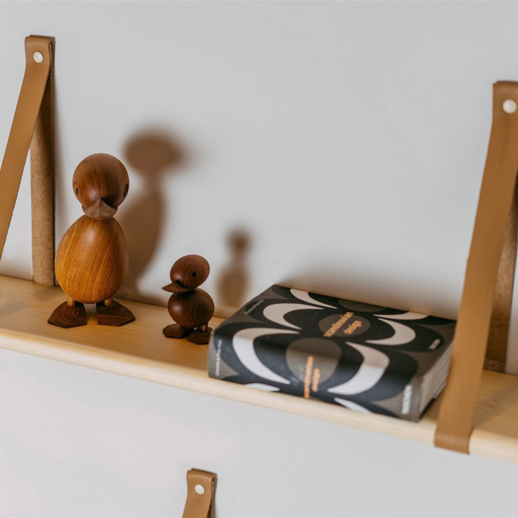 a 60 cm solid pine floating shelf with two light camel leather straps, shown in a soft, elegant close-up that highlights the wood grain and refined scandinavian detail