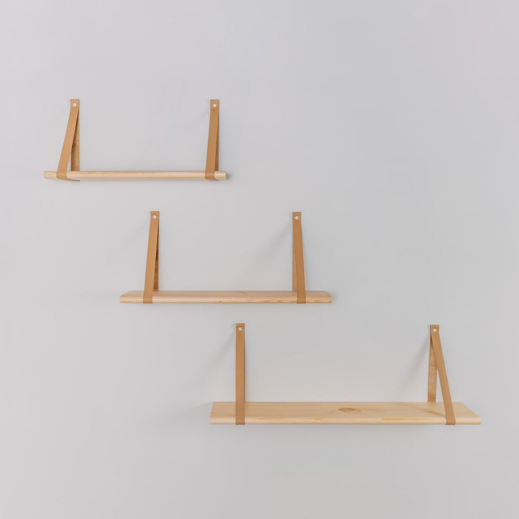 a floating pine shelf with leather straps holding a soft baby onesie in a cozy nursery setting