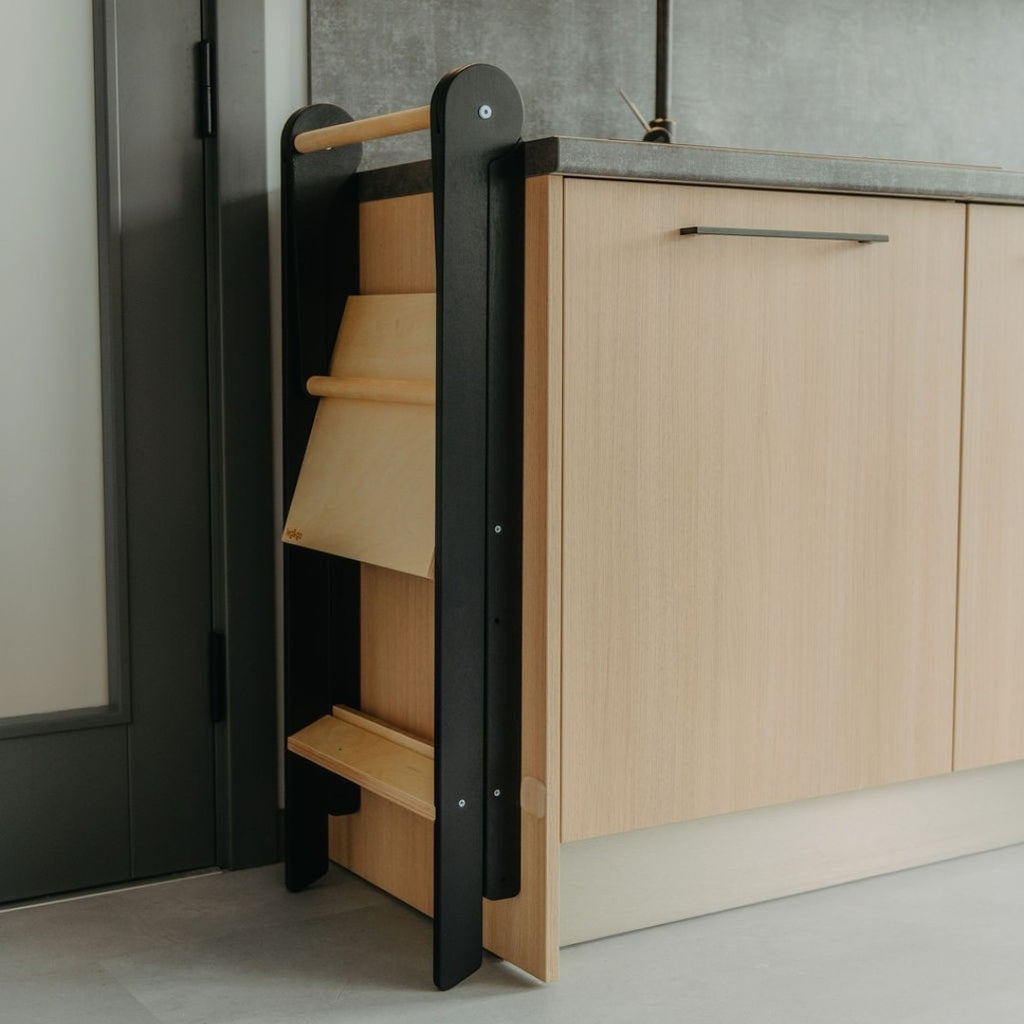 a soft-lit kitchen scene with a child safely standing at the counter in their foldable helper tower