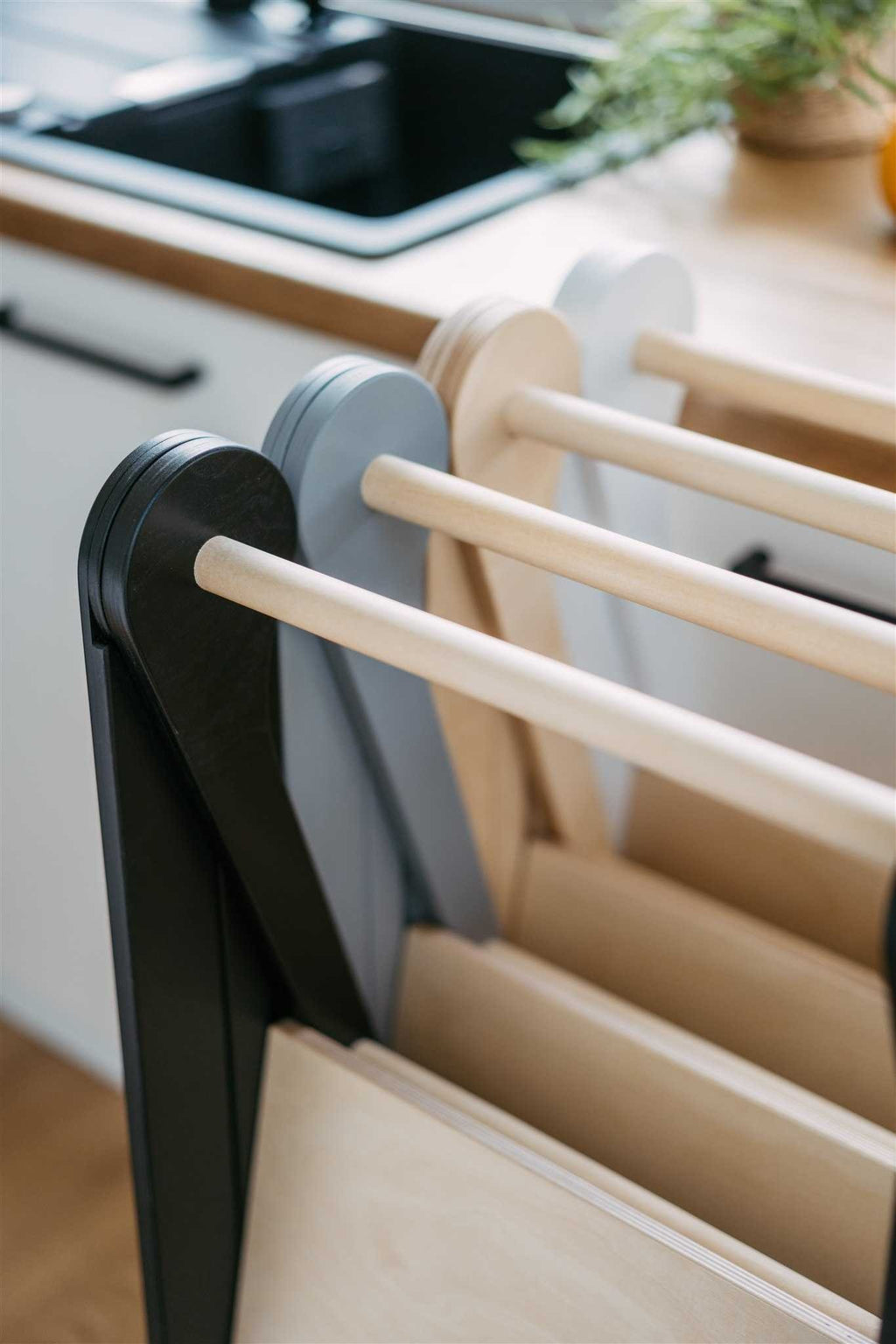 a child's hand gripping the birch safety rail of a foldable kitchen helper tower