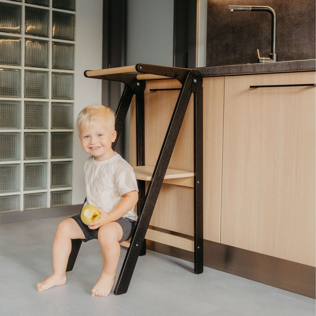 a child's hand on the sturdy birch safety rail of a folded kitchen tower