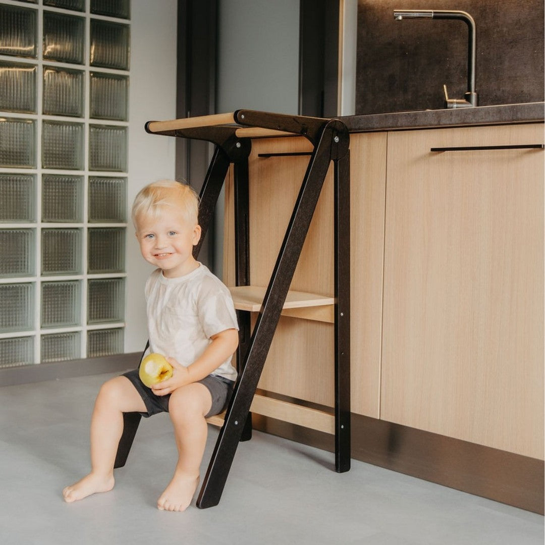 a child's hand on the sturdy birch safety rail of a folded kitchen tower
