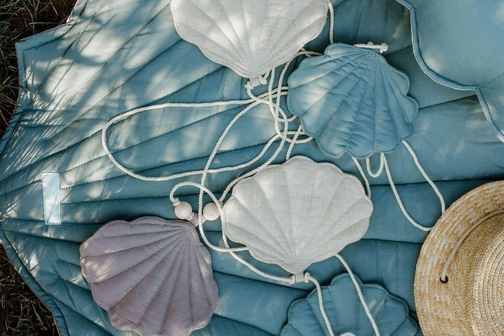 playful dusty blue shell garland with wooden beads, hanging in a sunlit nursery for a whimsical fairy-tale vibe