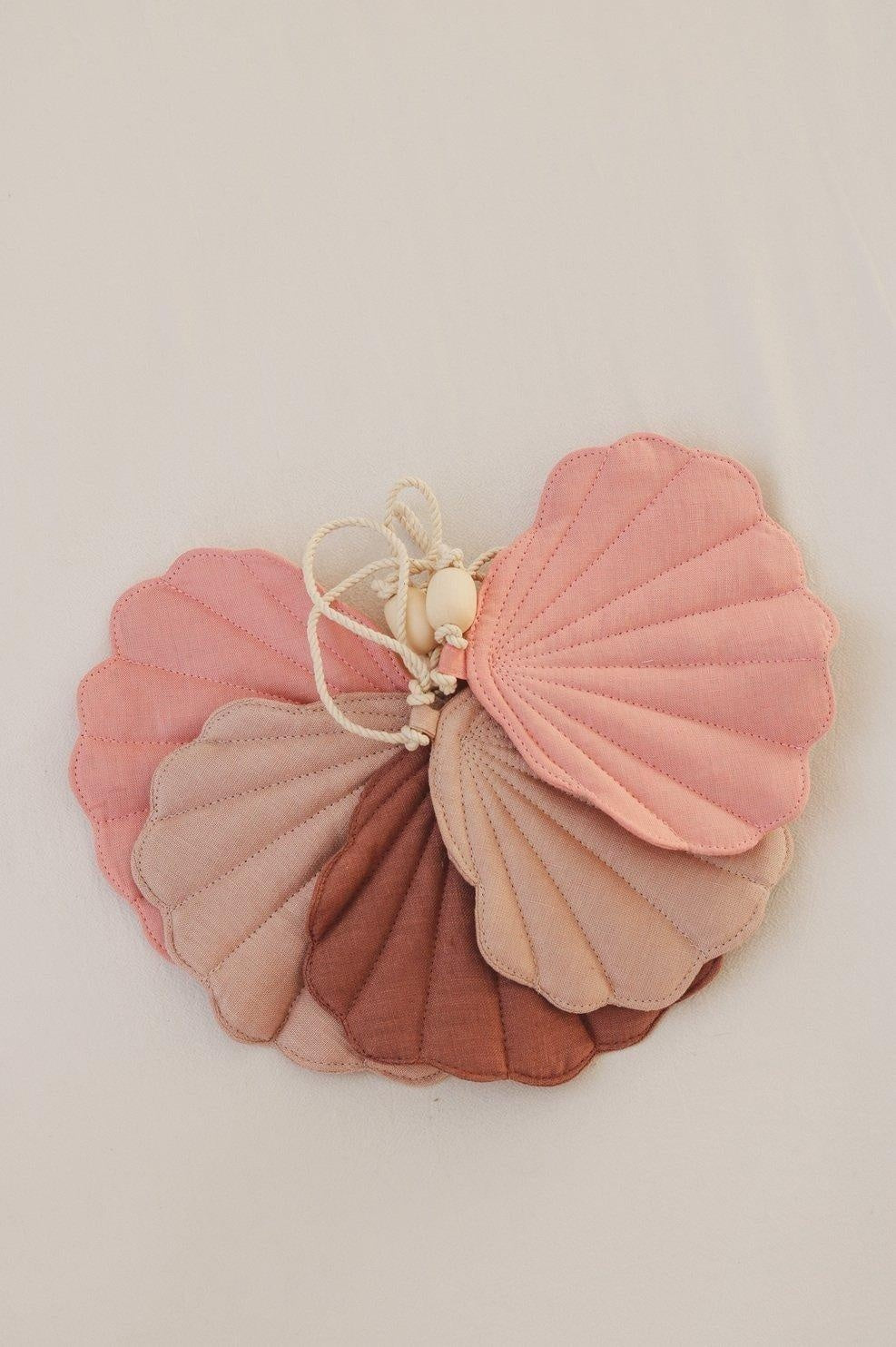 soft powder pink shell garland draped gently over a nursery crib with warm morning light