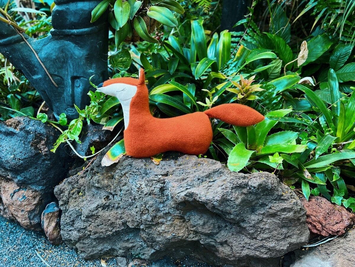 a playful handmade fox pillow mid-fluff, its forest red fur catching the light during a pretend blanket fort adventure