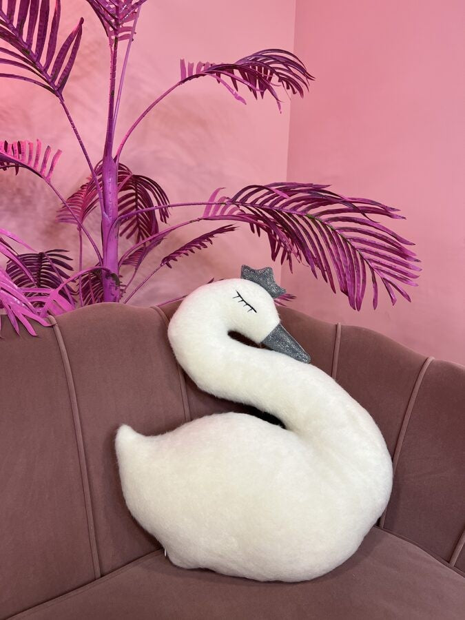 a playful handmade swan soft toy with a crown mid-waddle on a sunny yellow background