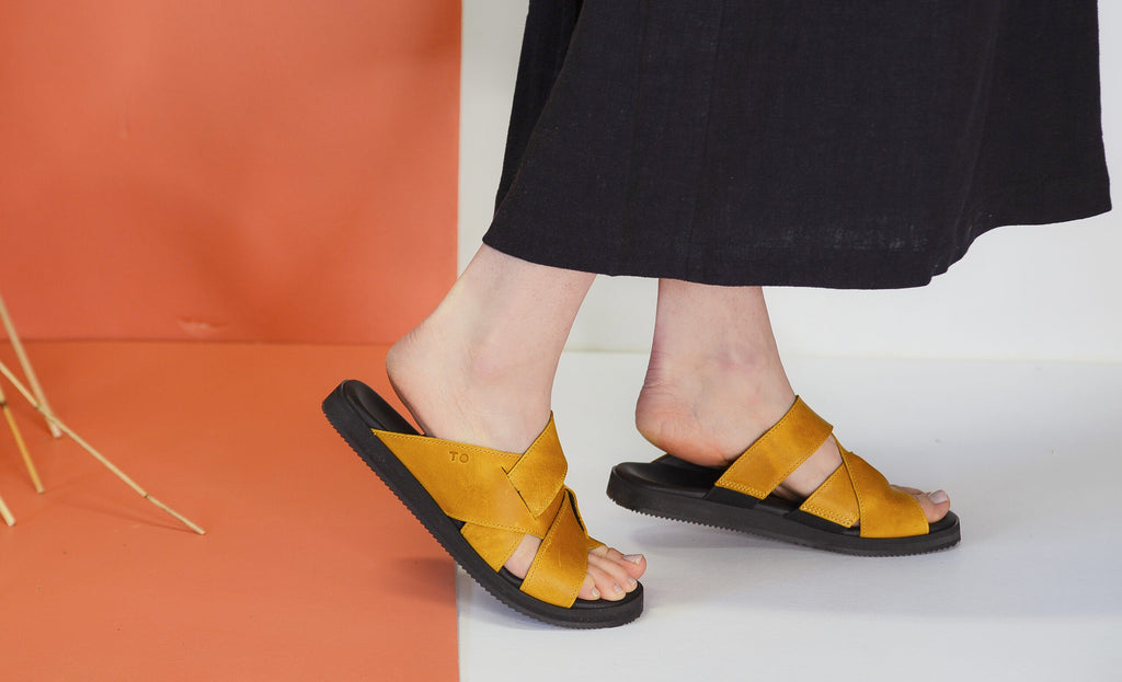 confident woman stepping forward in stylish ocre helsinki leather sandals on urban pavement