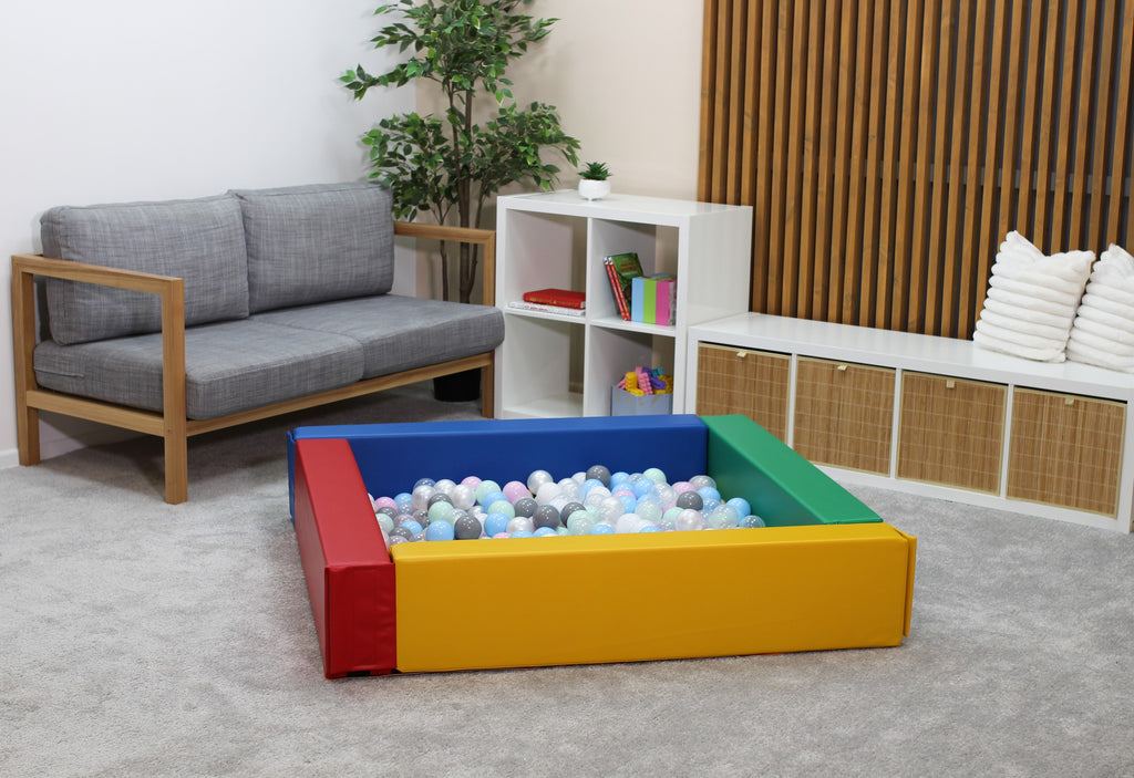 a child's hand reaching into a vibrant soft play ball pit filled with colorful plastic balls