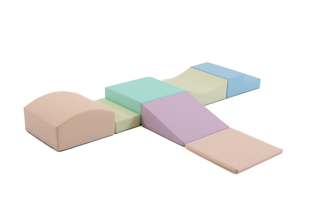a baby's hand reaching for a soft pastel foam block set on a clean white background