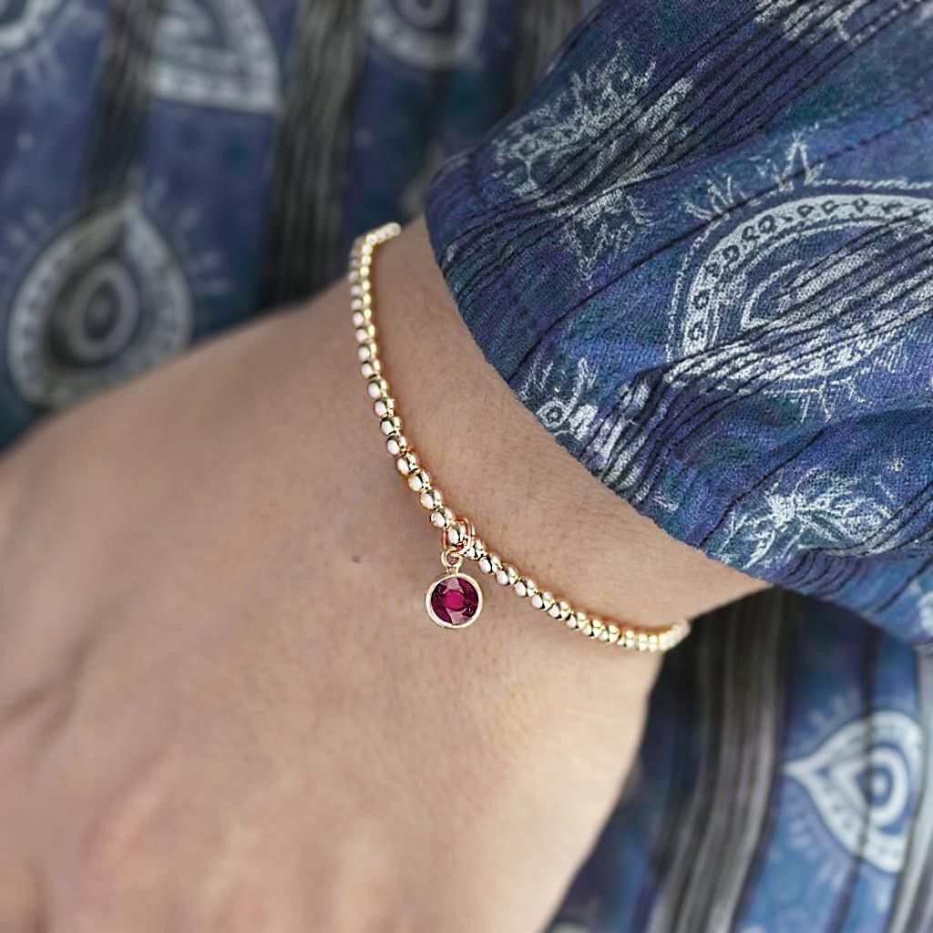 Gold bracelet with a red gemstone on a wrist against a blue fabric background a Sostter
