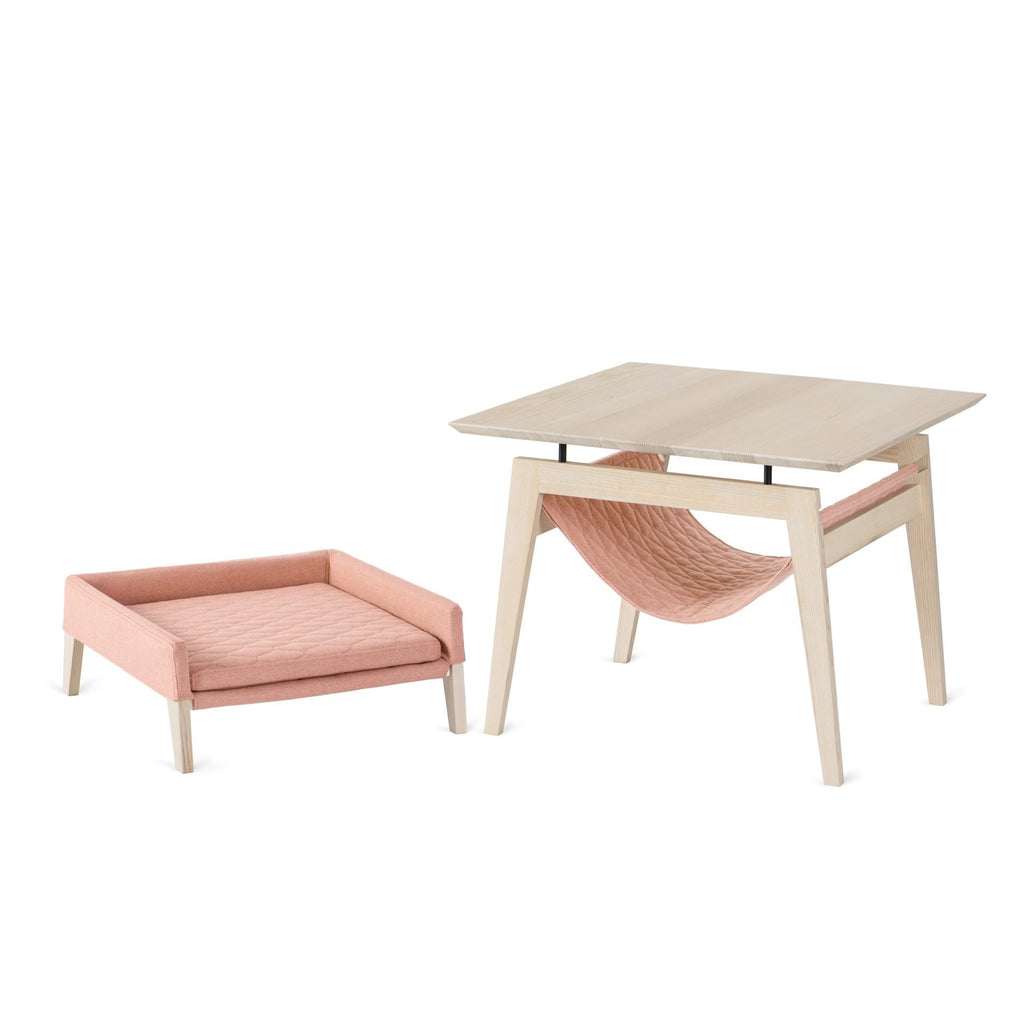 a soft raspberry cat bed nestled under a modern ash wood table in cozy morning light