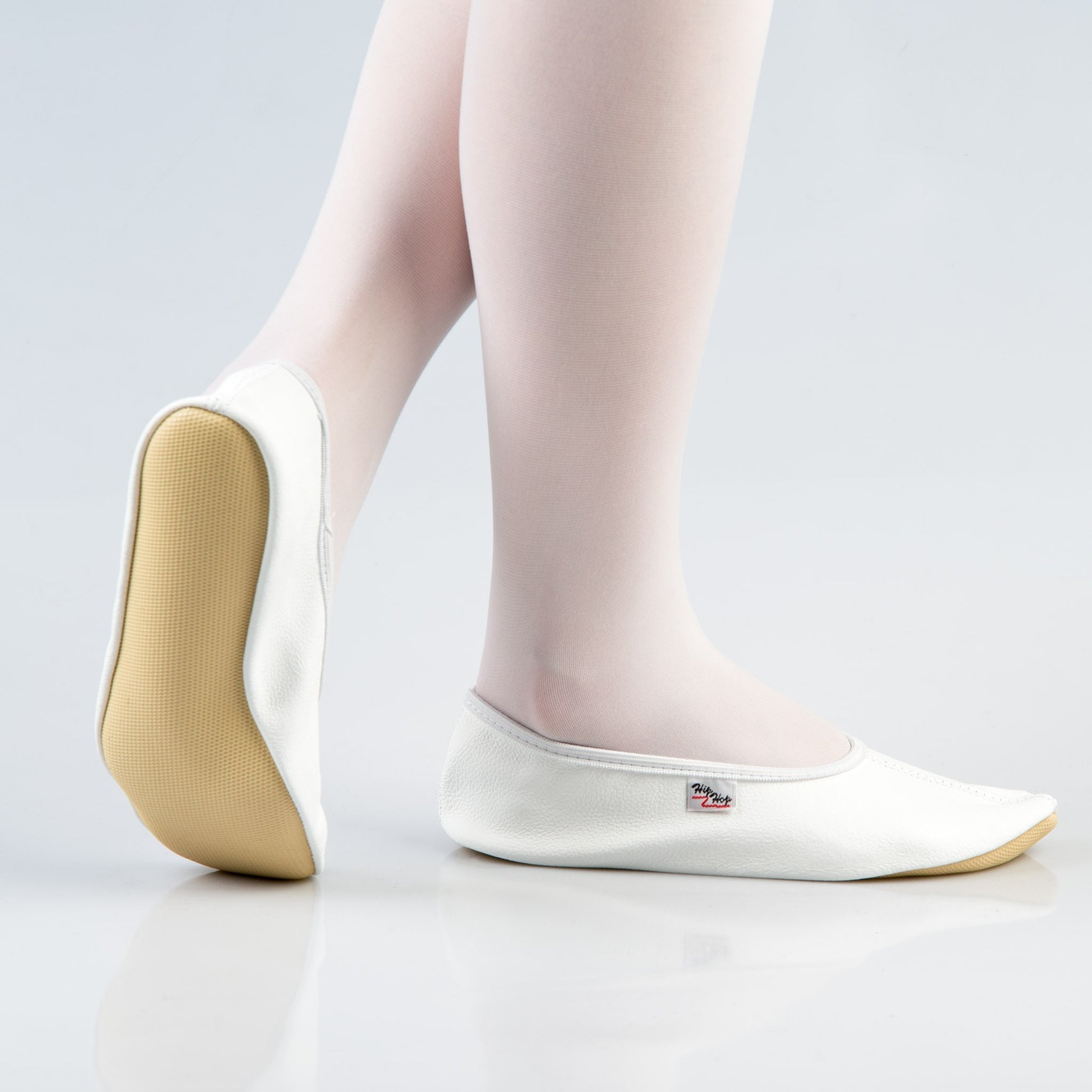 white leather gymnastics slippers with bold rubber sole on a dark studio floor