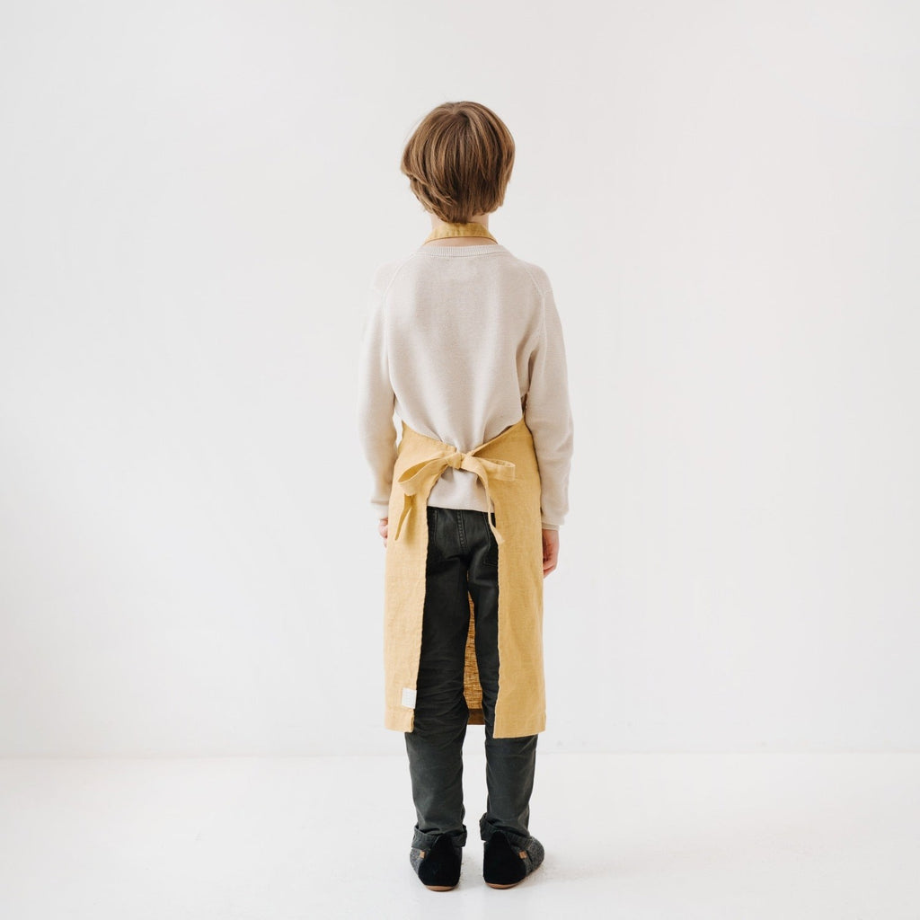 elegant honey linen kids apron on a wooden table, showcasing its refined texture and adjustable ties