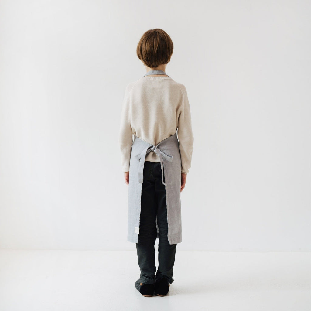 light grey kids apron with adjustable ties and a front pocket for holding kitchen tools