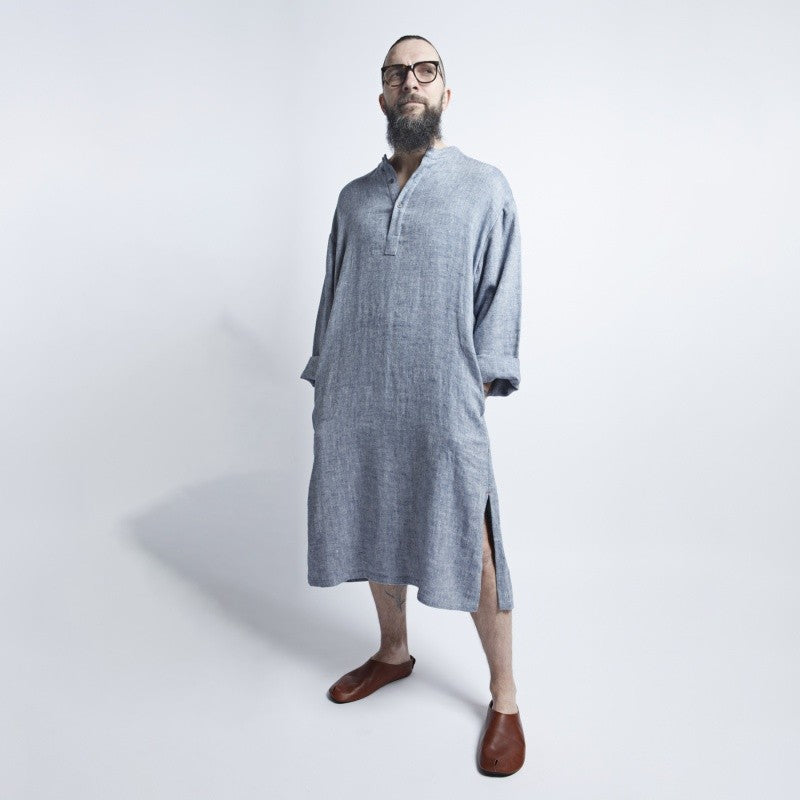 a confident man in a blue gray linen dress standing boldly against an urban backdrop