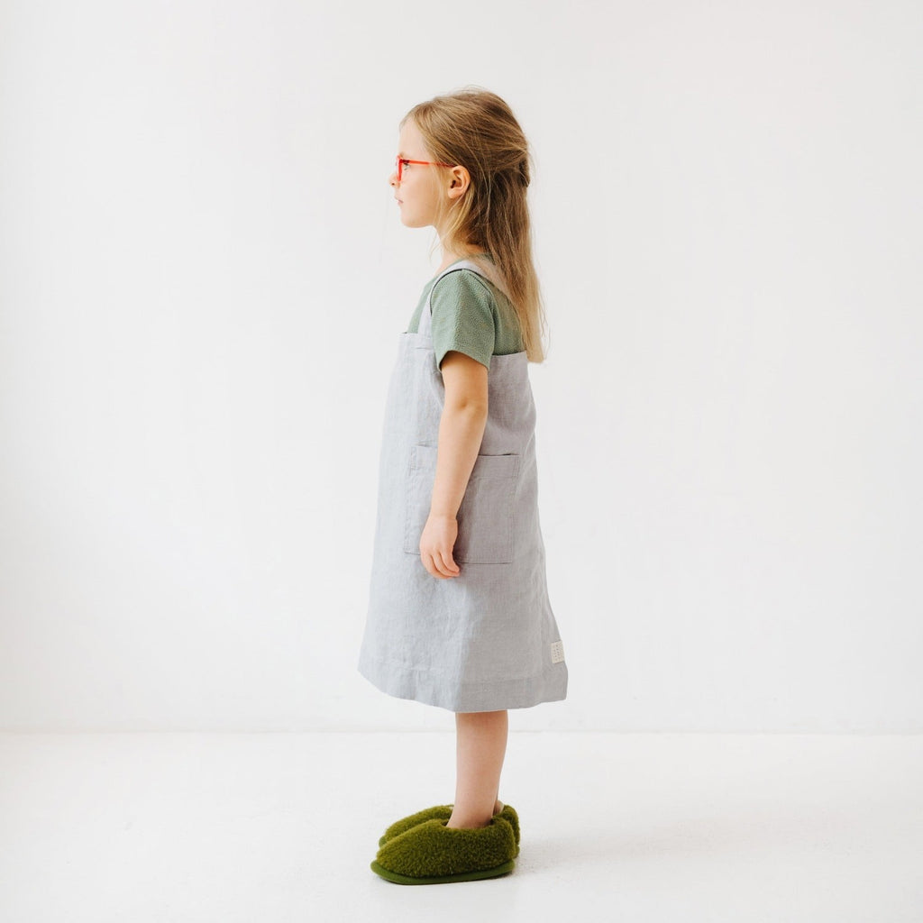 a playful child chef in a light grey linen pinafore apron, laughing while holding a wooden spoon