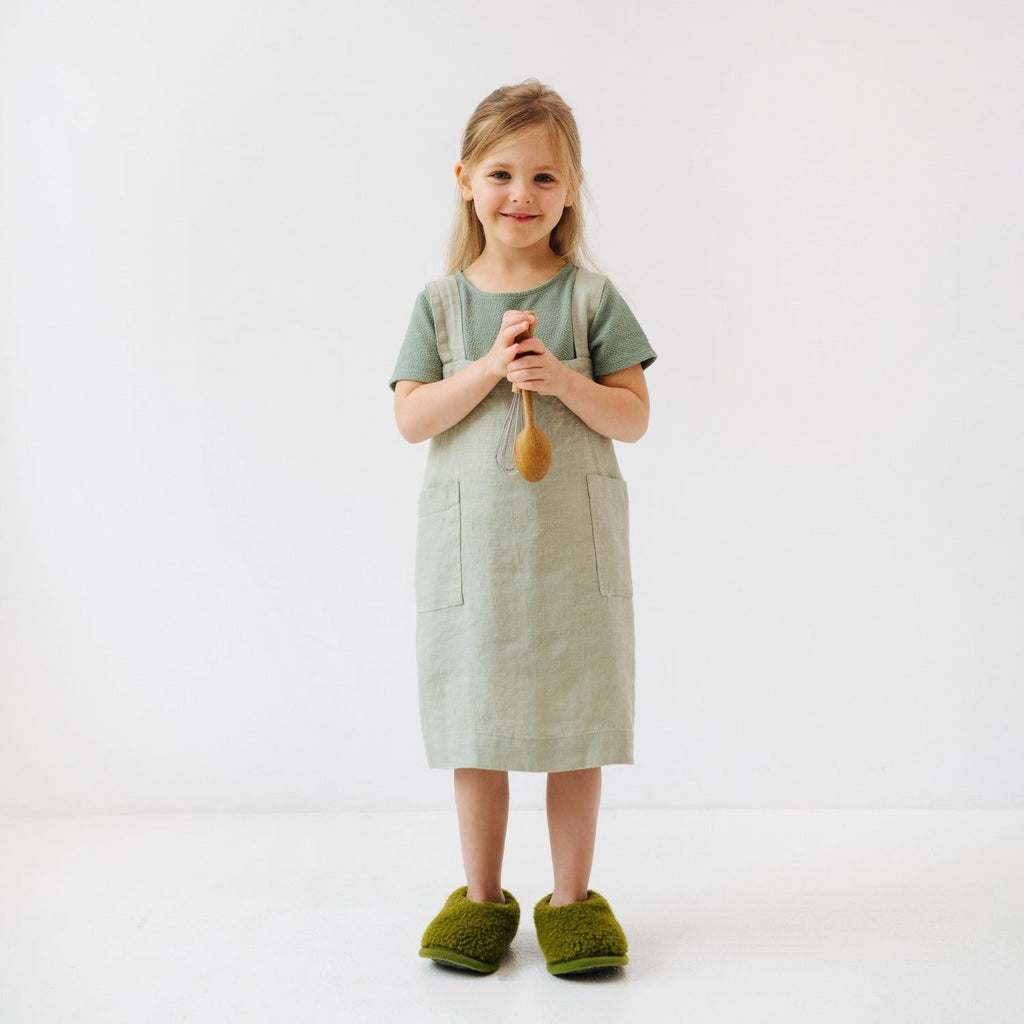 close-up of a child's sage linen apron pockets holding kitchen utensils